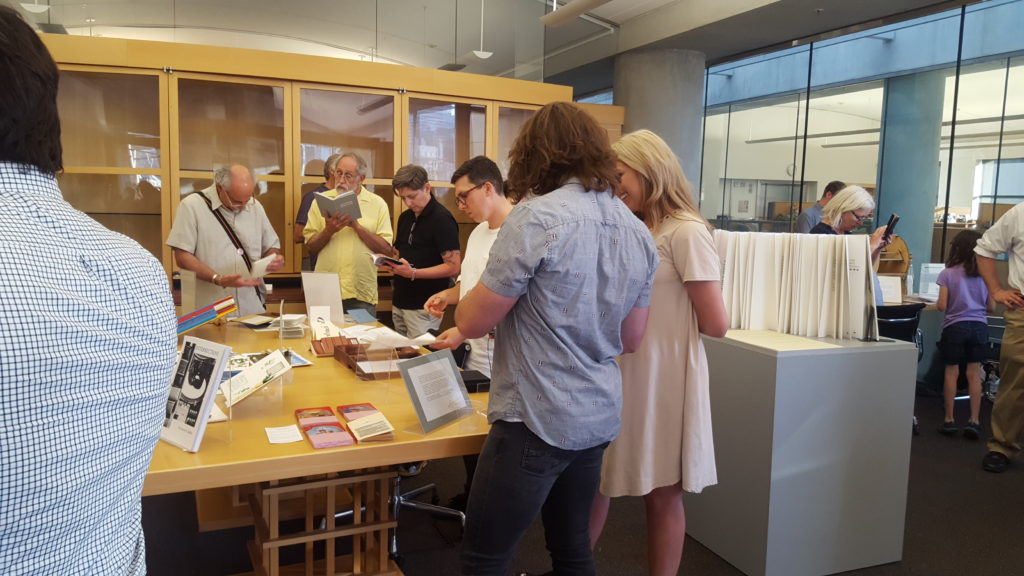 A group of people look at and touch books on a table in a library exhibit.