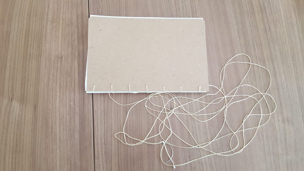 An incomplete coptic stitch book with thread hanging from the side.