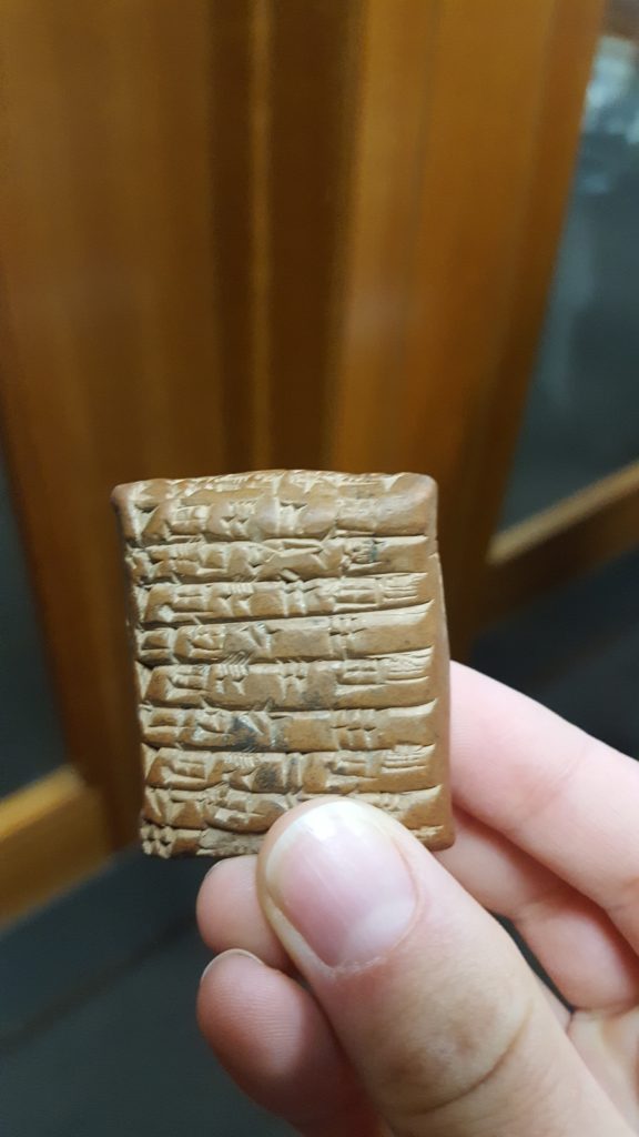 A Sumerian clay tablet held in someone's hand, the inscriptions on the tablet visible.