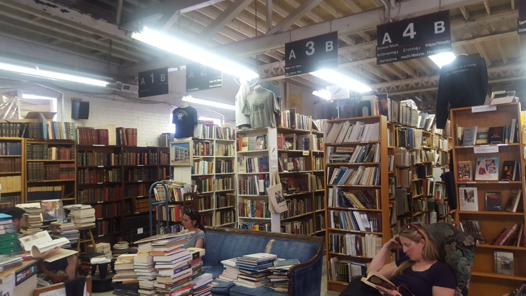A room filled with bookshelves, and books stacked on top of a table.