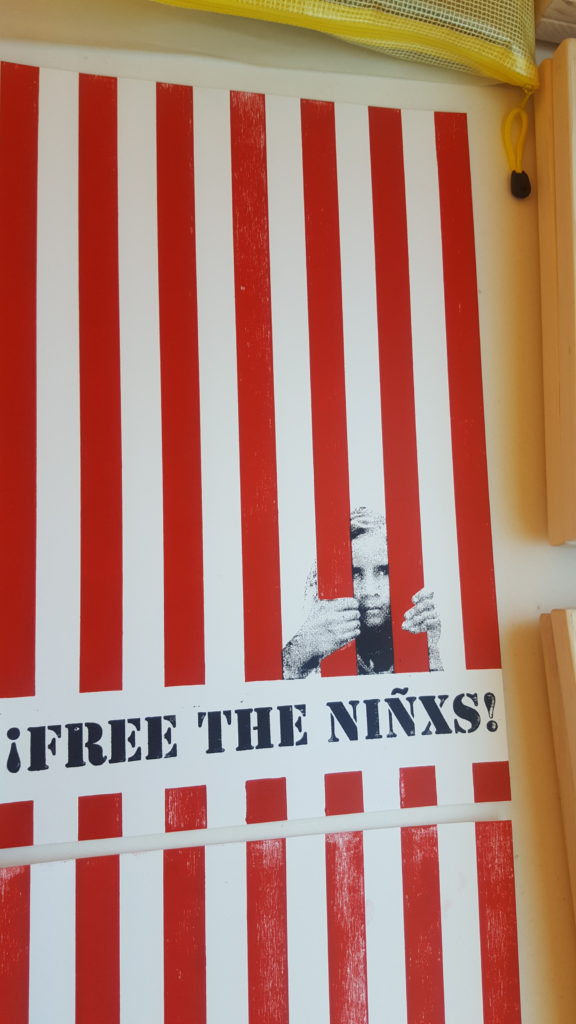 A poster with vertical red bars, and a child grasping behind one of the bars. The text reads "Free the Ninxs!"