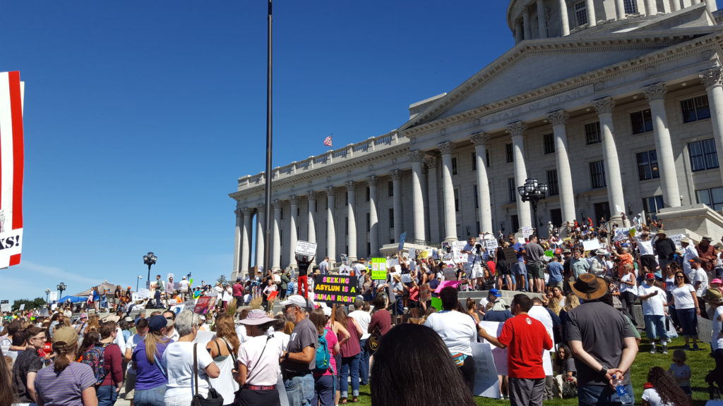 A group of people stand with protest signs in front of the rotunda at the Utah State Capitol.