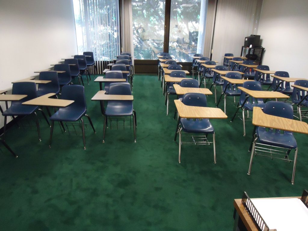 Empty chairs lined up in a row in an empty classroom.