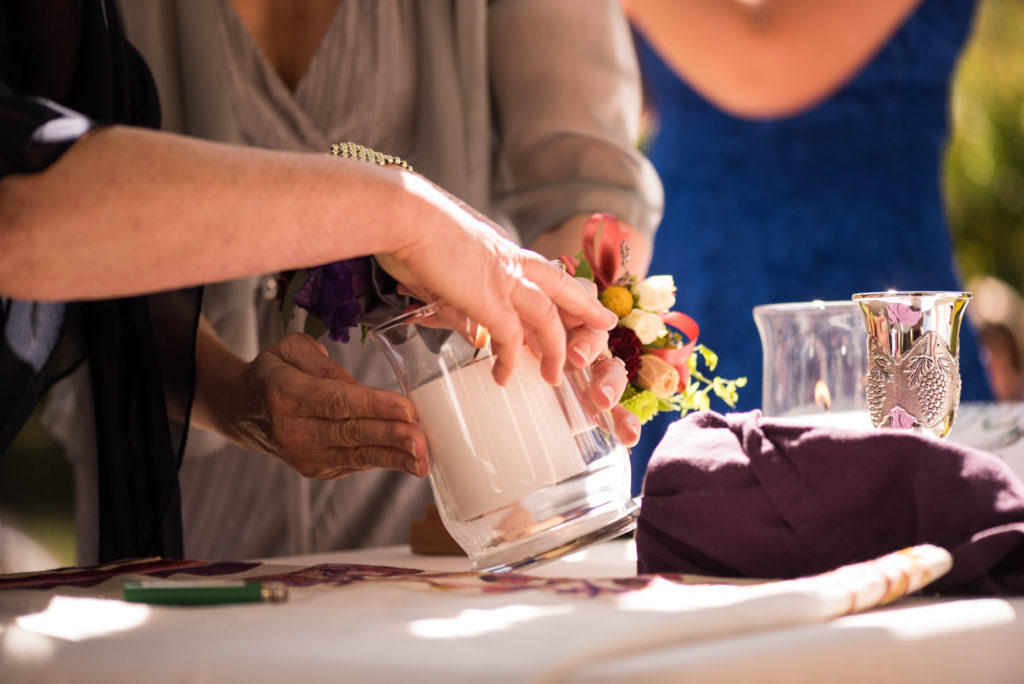 A hand holds a candle while another person attempts to light the candle.