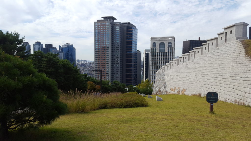 A view of Seoul with an old brick wall in teh front and skyrises in the background.