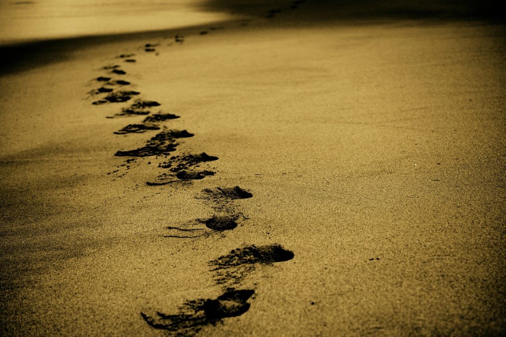 An expanse of sand, dotted by footprints marking a path.