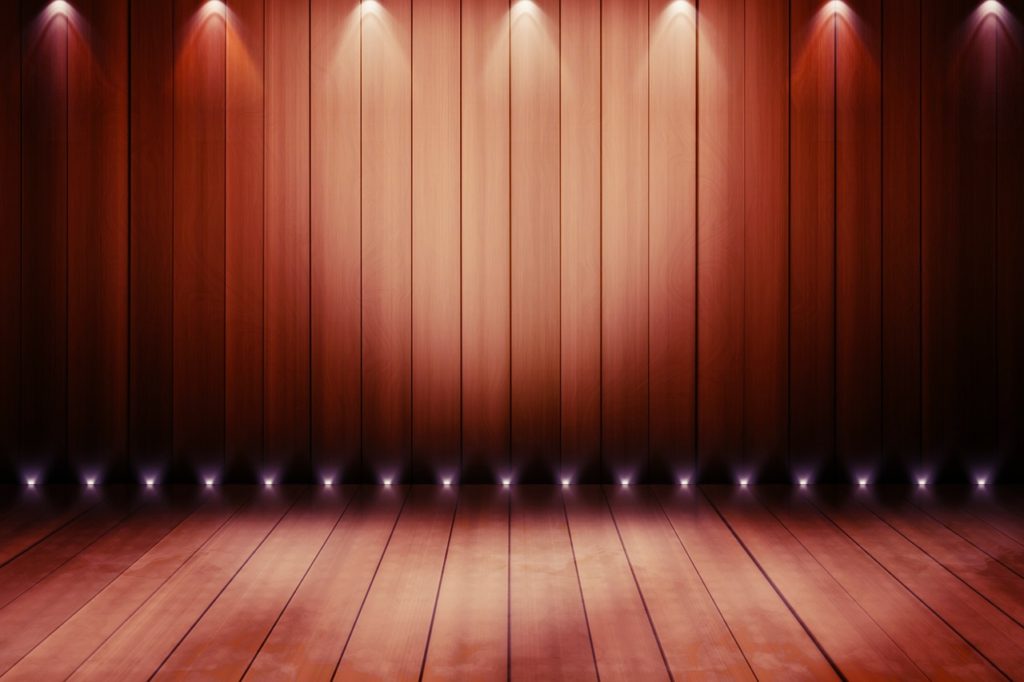  An empty stage with spotlights shining on to wooden floor.