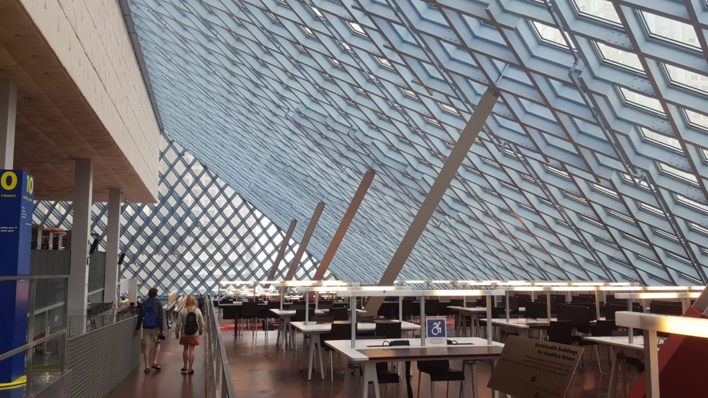 The interior of the Seattle Public Library: a sloped and angled ceiling  with natural light flooding the rows of desks beneath.